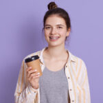 Smiling female with hair bun holding take away coffee in hands,